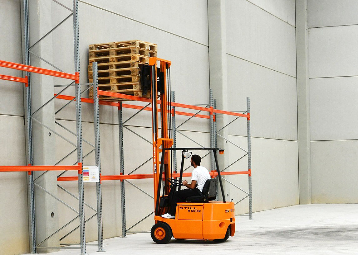 forklift stacking pallets on metal shelves